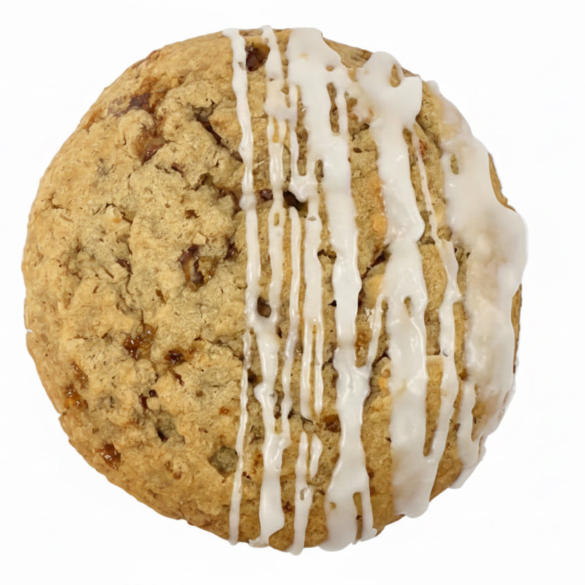 Top-down view of a round, golden-brown gluten-free cookie with a soft, crumbly texture and visible bits throughout, drizzled with white icing on one half against a clean white background.
